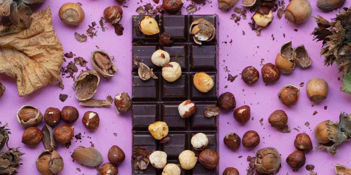 Purple background with a block of chocolate and scattered nuts and plants.