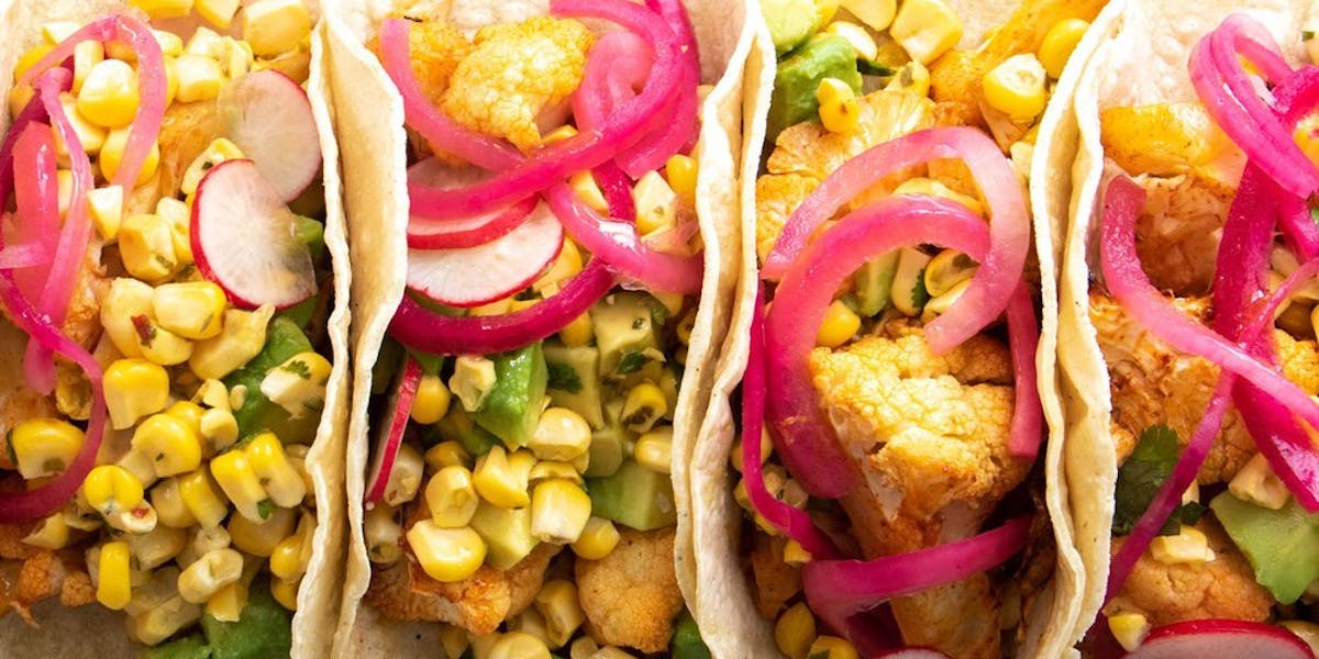 Four vegan tacos filled with sweetcorn, avocado and onion