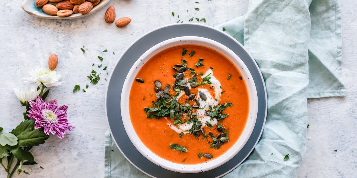 tomato and pumpkin soup on table with almonds and flowers