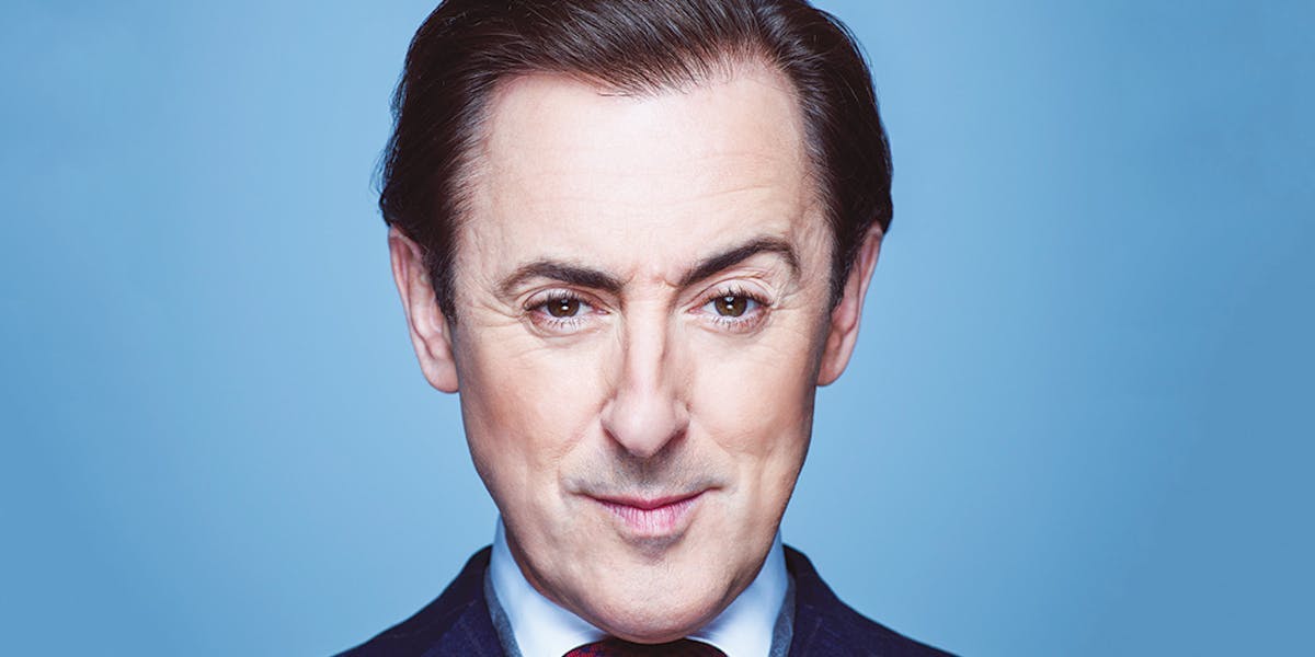 Alan Cumming head shot in front of a blue background