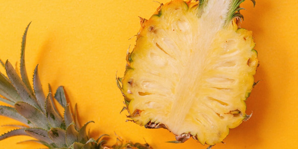 Pineapple cut in half lengthways on an orange background 