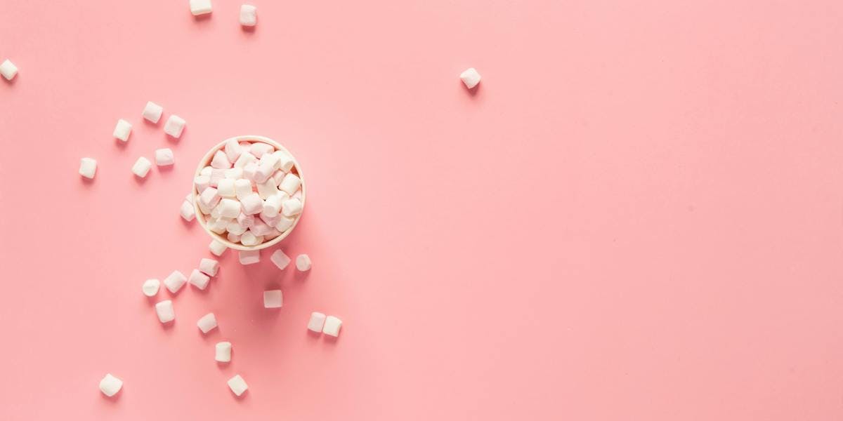 pink background with mini marshmallows in cup and scattered across surface