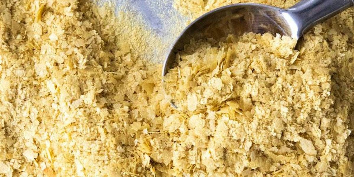 Birdseye view of nutritional yeast flakes with a silver spoon scooping them up from the table.