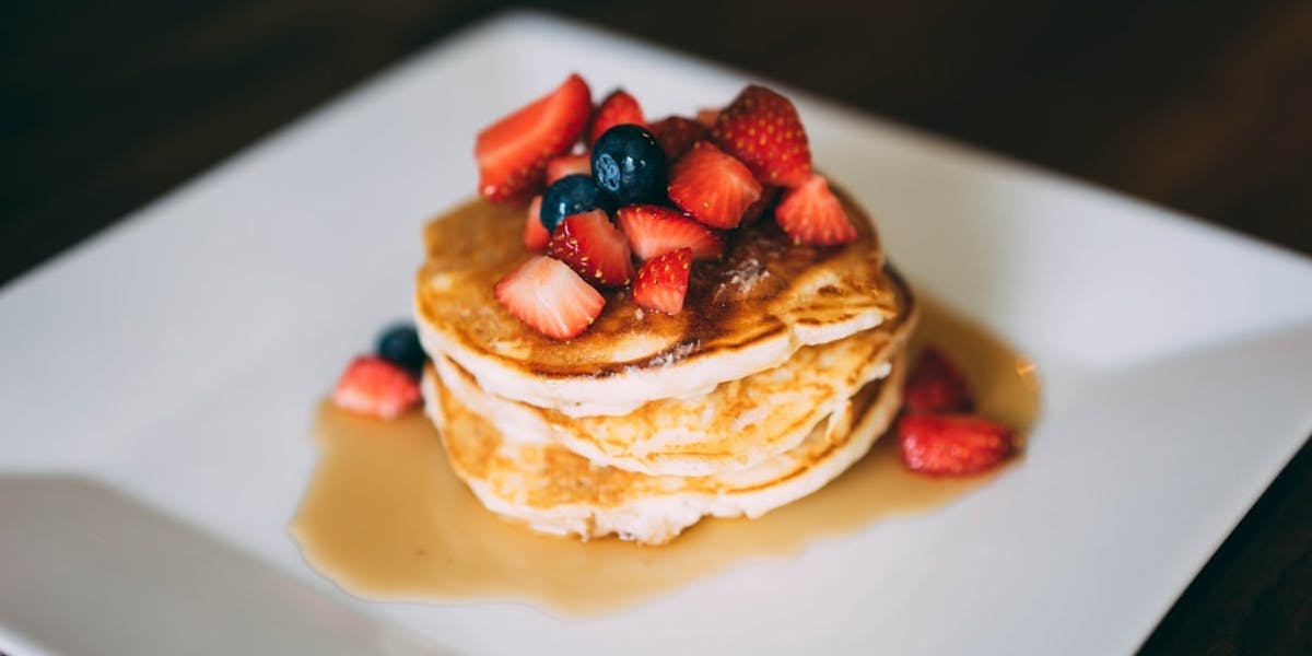 stack of pancakes with fruit and syrup