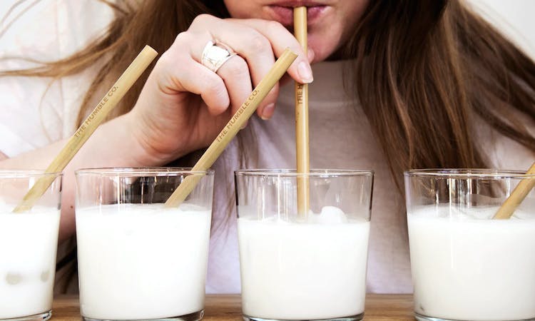 A person drinking 4 glasses of milk through straws