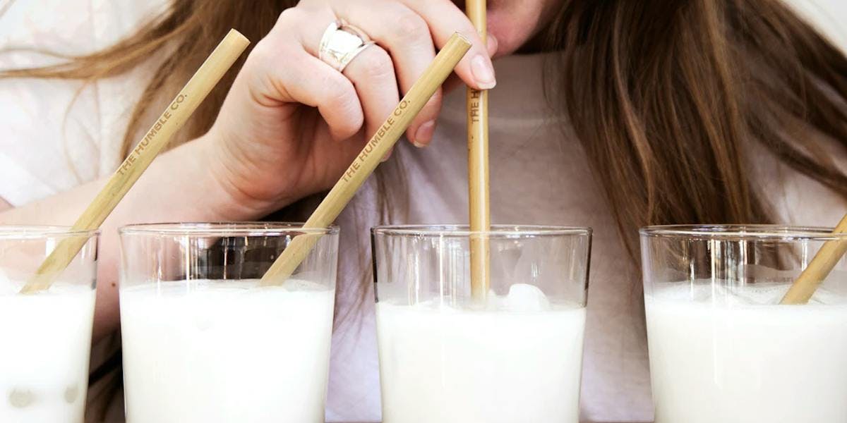 A person drinking 4 glasses of milk through straws