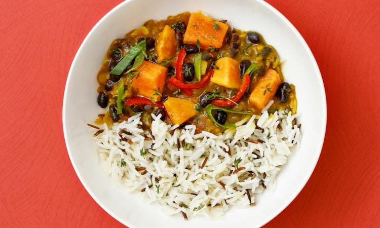 Sweet potato black bean curry in white bowl and red background