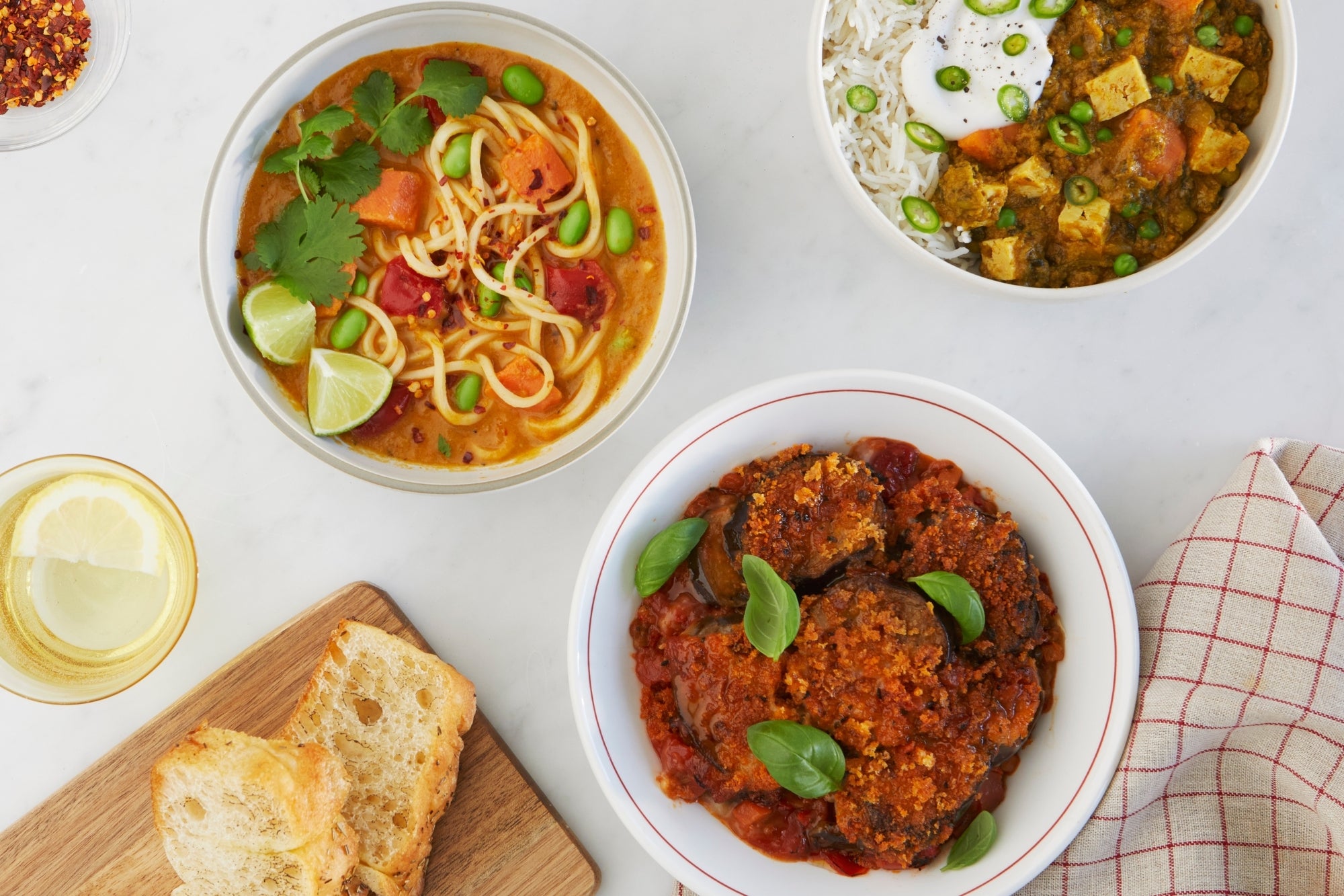 Assorted dishes including a bowl of noodle soup, a plate of curry, and bread on a white surface.